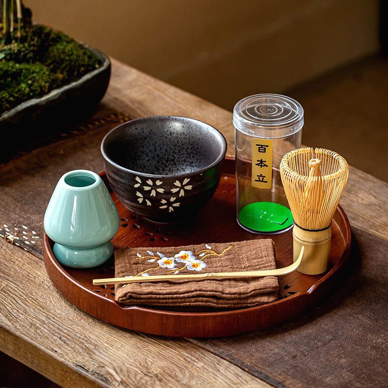 Kit matcha sur plateau rond avec bol noir à fleurs, fouet et porte-fouet vert