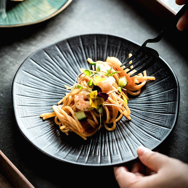 Assiette japonaise Nikkō noire garnie de pâtes aux légumes, tenue d'une main