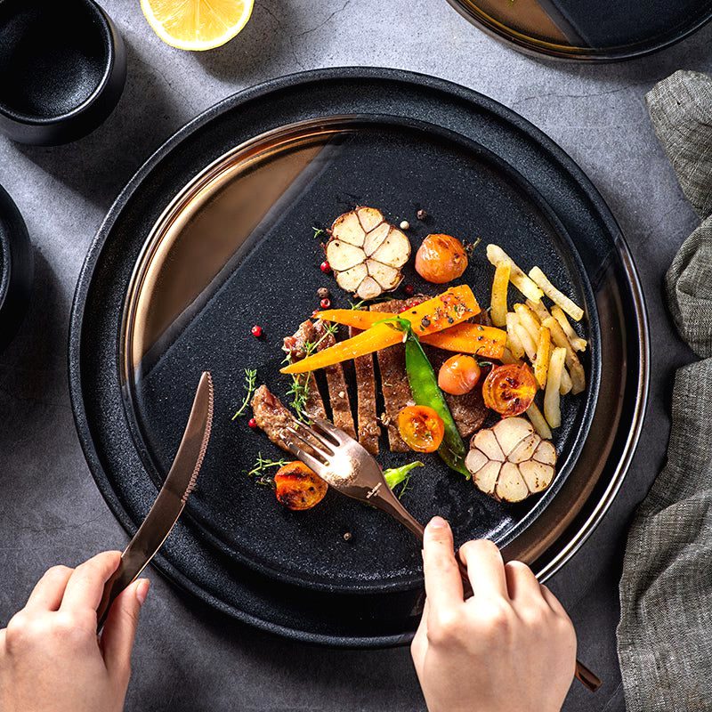 Assiette japonaise Yuna noir et or garnie de viande et frites, couteau et fourchette en main