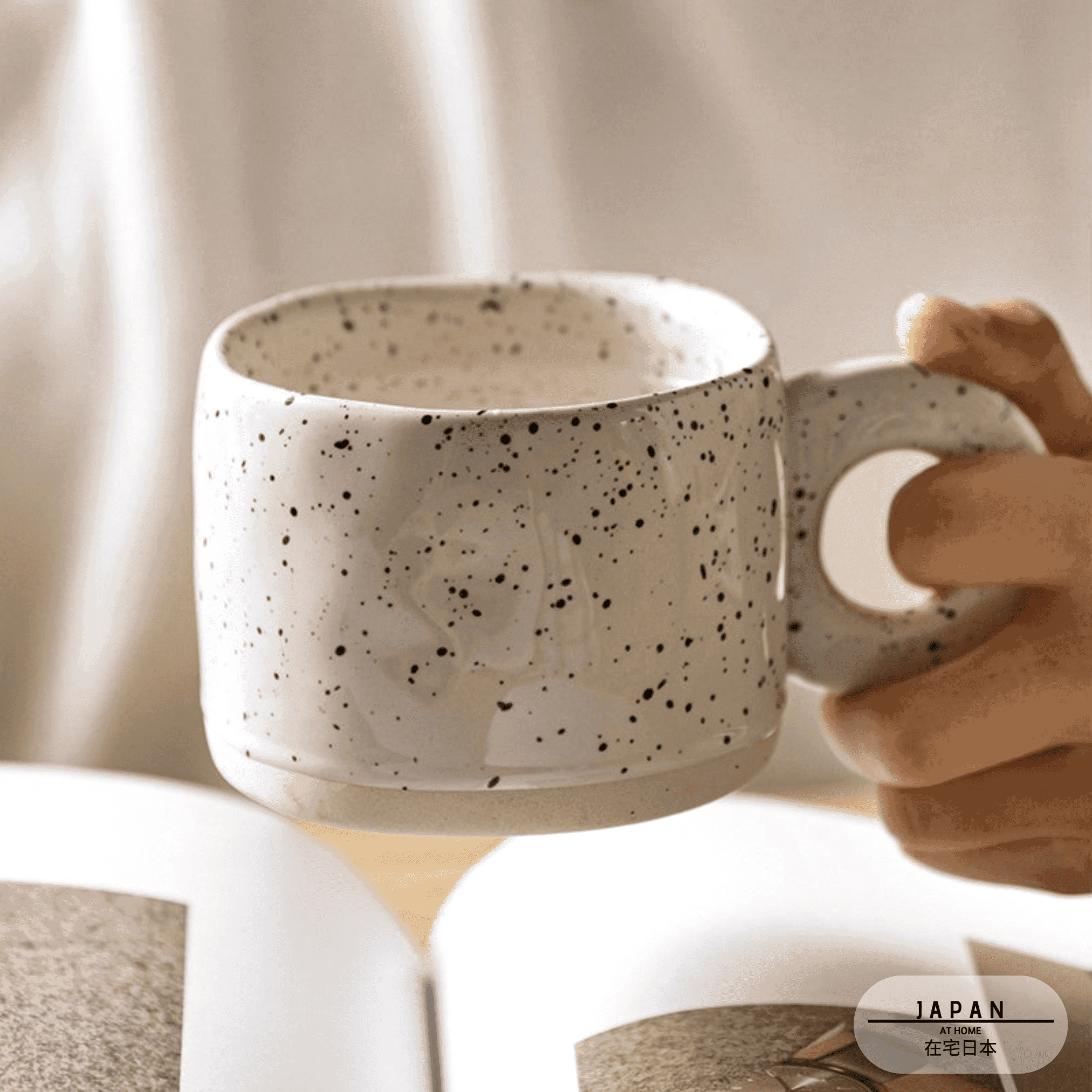 Tasse Nebula blanc cassé tenue par l'anse au-dessus d'un livre
