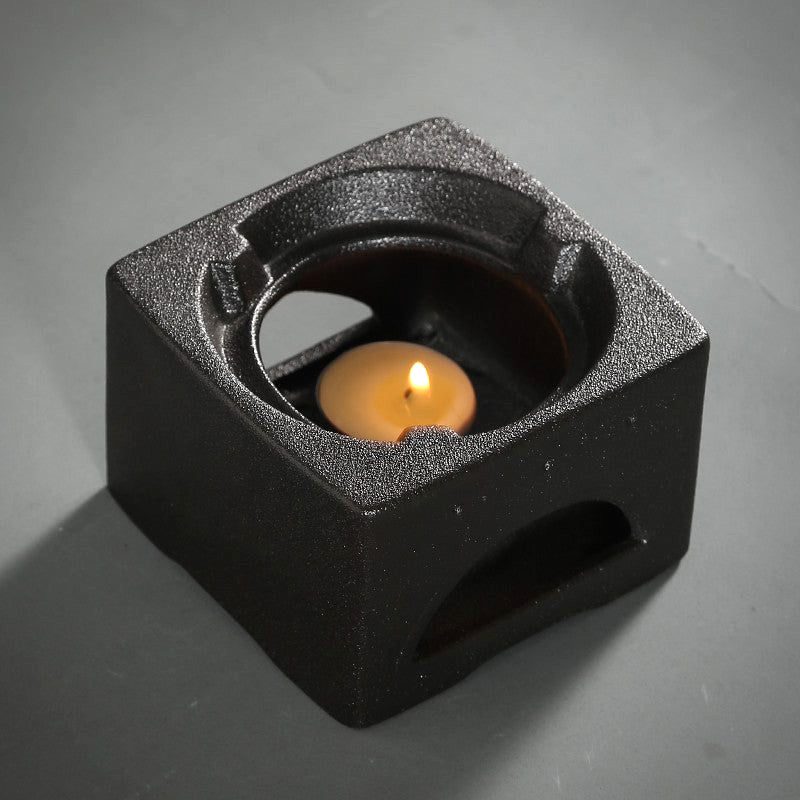 Réchaud noir de la théière avec une bougie allumée, vue de trois quarts