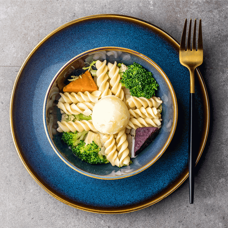 Bol Tatsuzo bleu garni de pâtes posé sur une assiette, vue de dessus