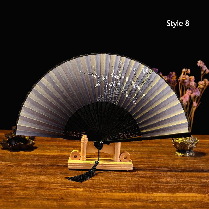 Éventail japonais en satin gris foncé à monture noire posé sur un support