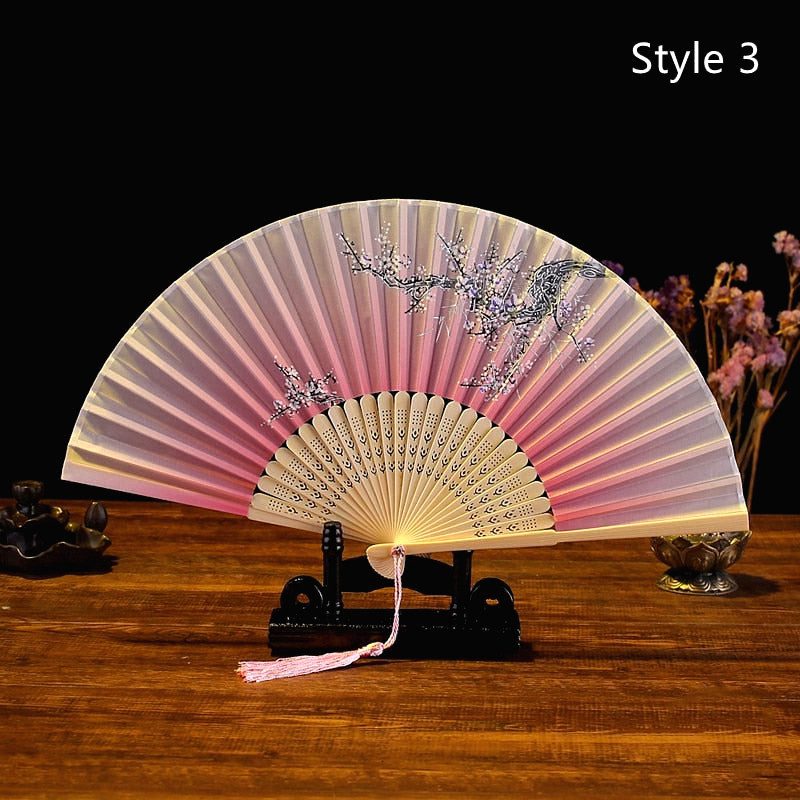Éventail japonais en satin rose pâle ouvert sur un support, branche gris bleu