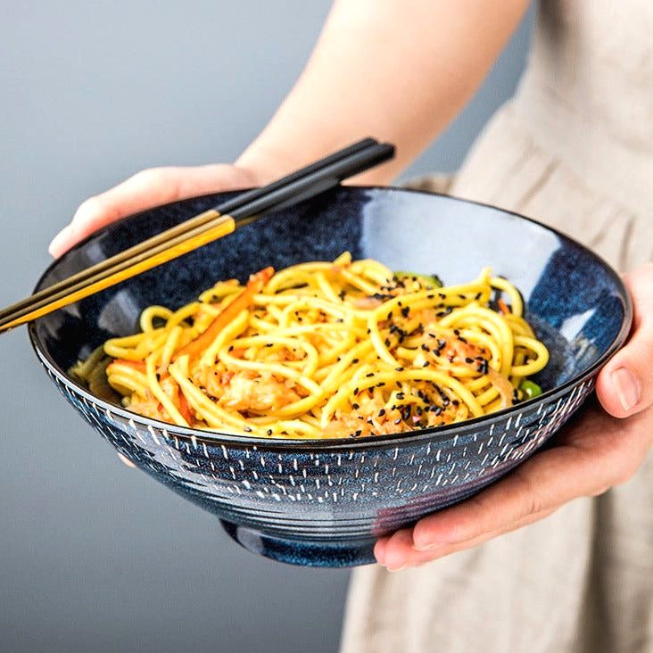 Bol à ramen Miyasato bleu rempli de nouilles sautées, baguettes en main
