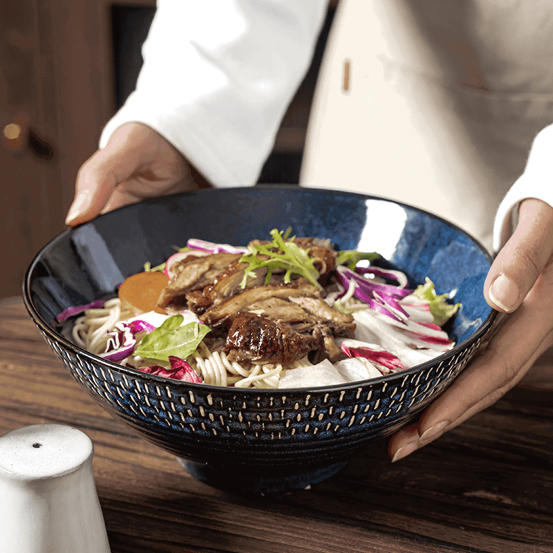 Bol à ramen Miyasato bleu garni de viande et de légumes, tenu à deux mains