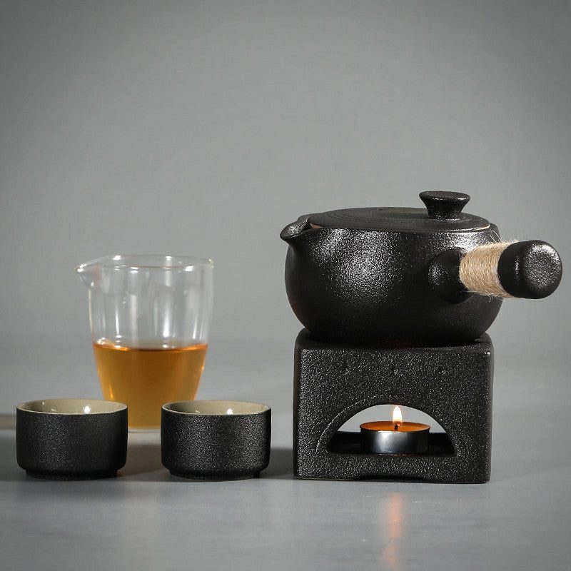 Théière noire sur réchaud avec deux tasses et un pichet de thé