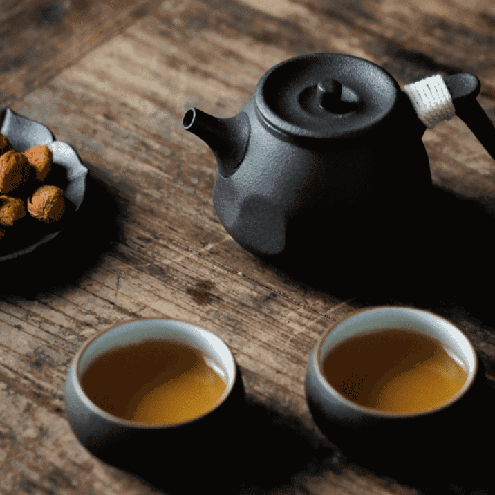 Théière Fukui noire et deux tasses remplies de thé sur une table en bois