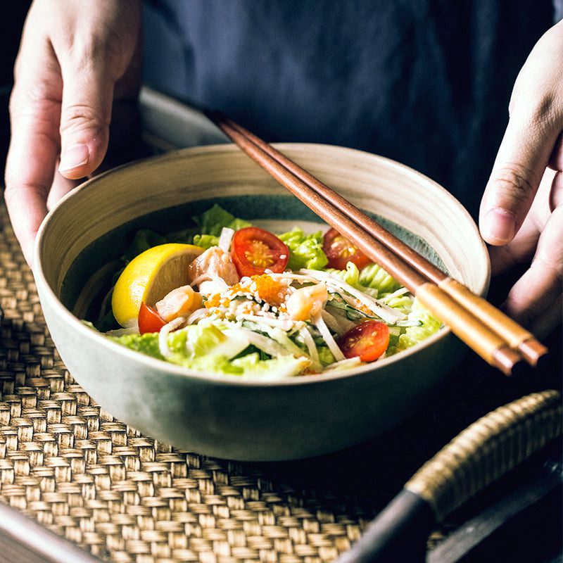 Bol Kugo vert rempli de salade, tenu à deux mains avec baguettes