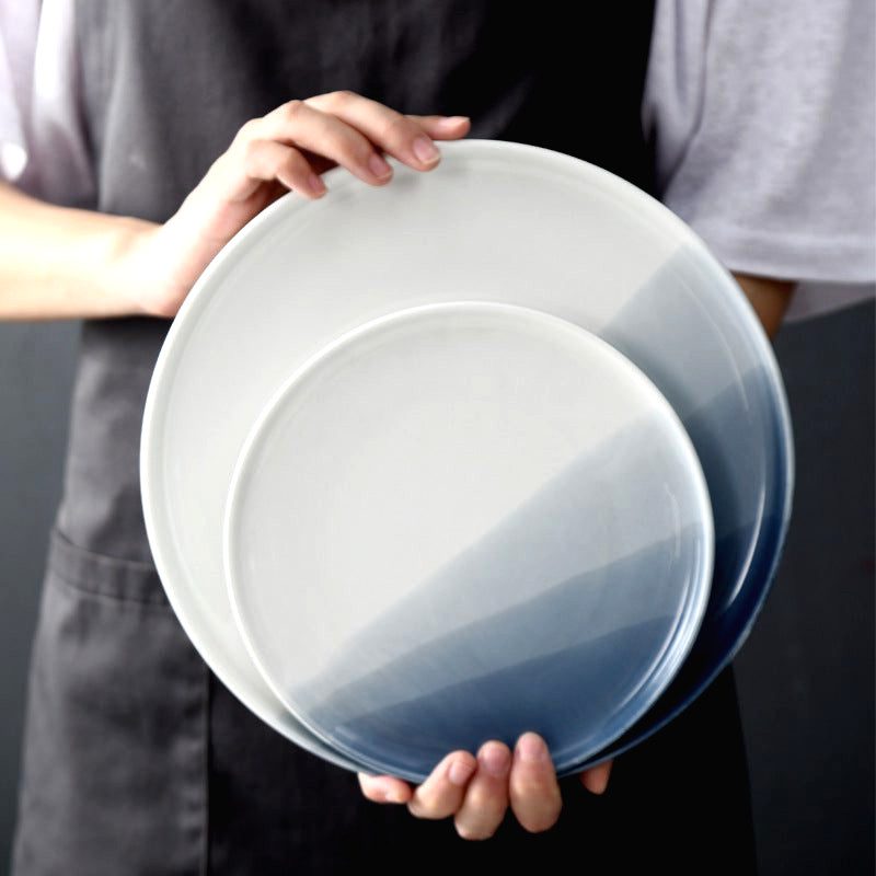 Deux assiettes japonaises Benjiro blanc et bleu tenues en main, la petite devant la grande