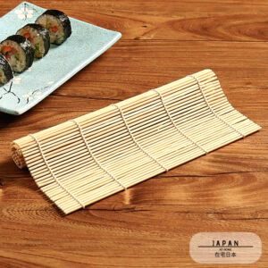 Natte à sushi en bambou déroulée sur une table, makis en arrière-plan