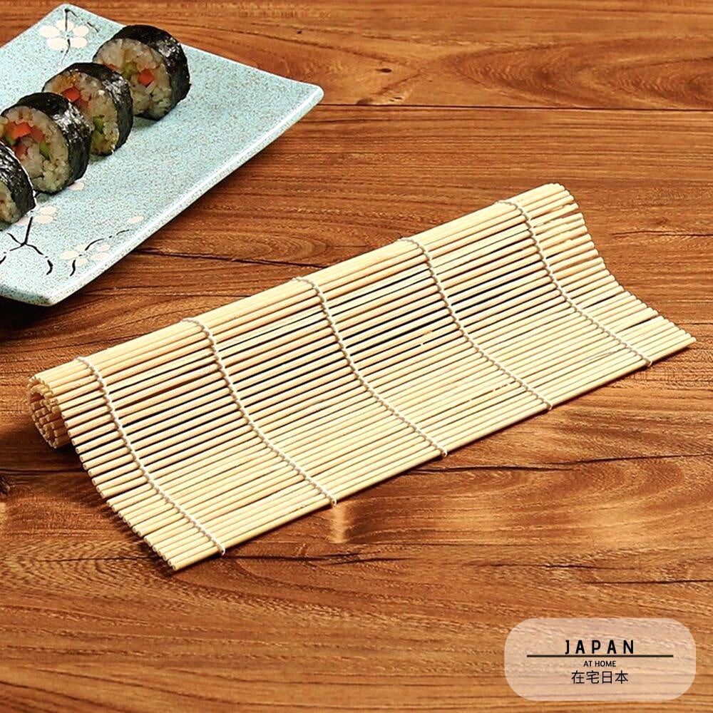 Natte à sushi en bambou déroulée sur une table, makis en arrière-plan