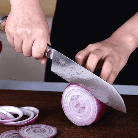 Couteau à sushi en acier tranchant un oignon rouge, tenu en main