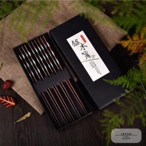 Coffret de baguettes en bois sombre ouvert sur un tissu, feuillage autour