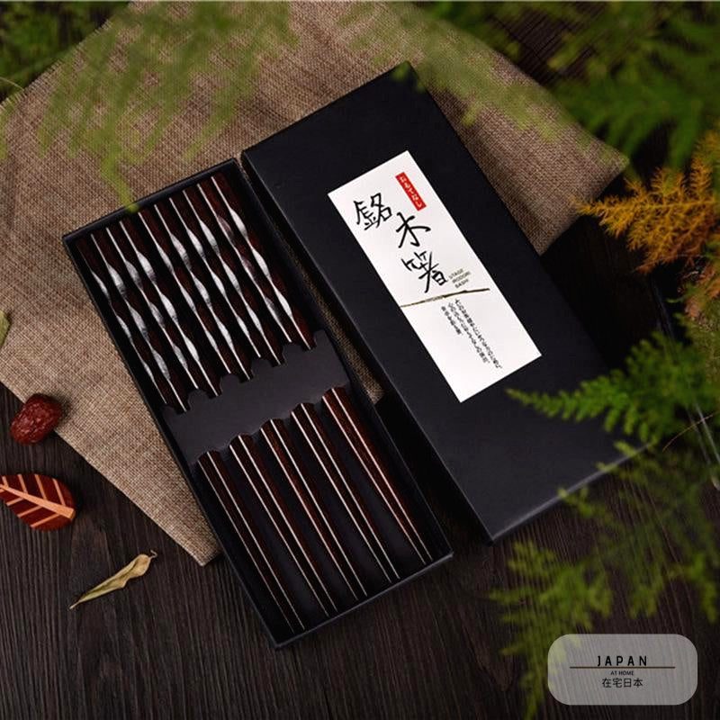 Coffret de baguettes en bois sombre ouvert sur un tissu, feuillage autour