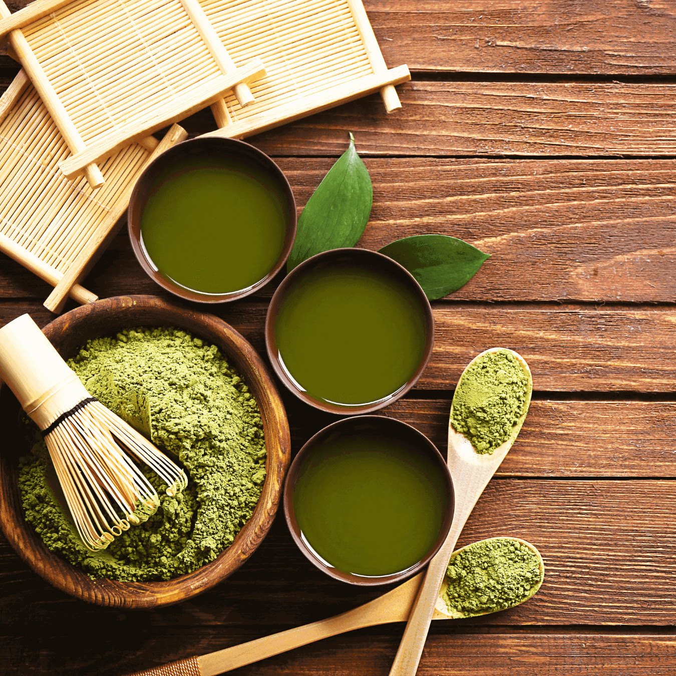 Trois bols de matcha préparé et un bol de poudre sur une table avec fouet