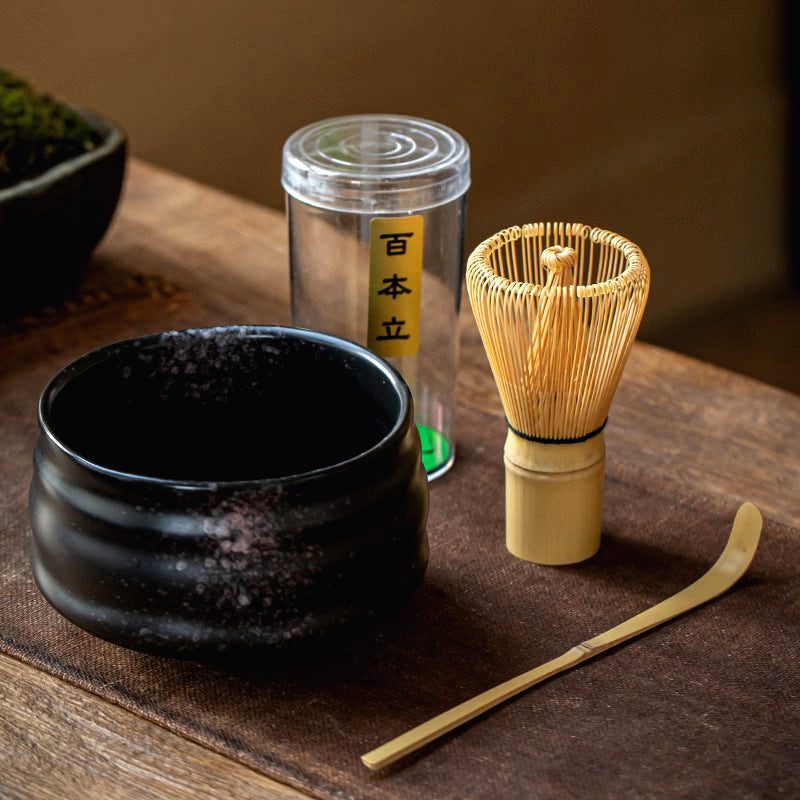 Kit matcha avec bol noir, fouet en bambou et cuillère sur une table en bois