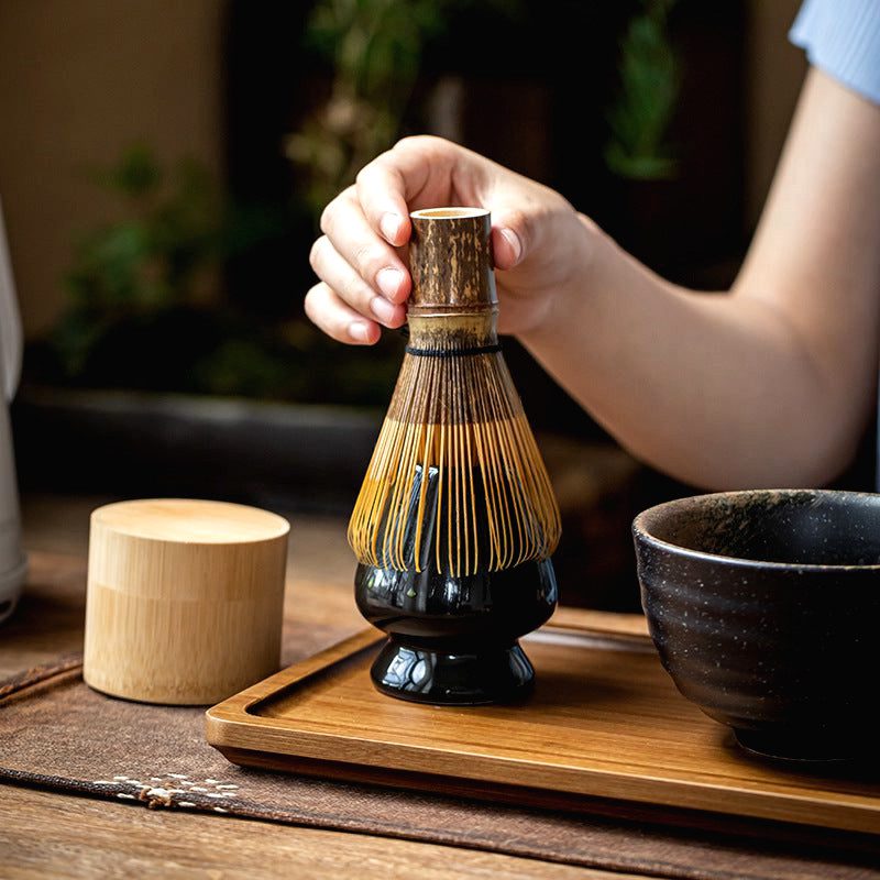 Fouet matcha posé sur son porte-fouet noir par une main, bol noir à côté