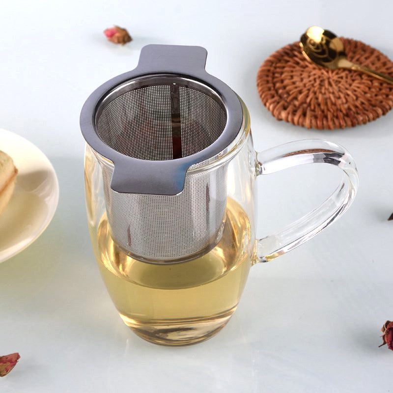 Infuseur à thé en inox posé sur une tasse transparente remplie de thé