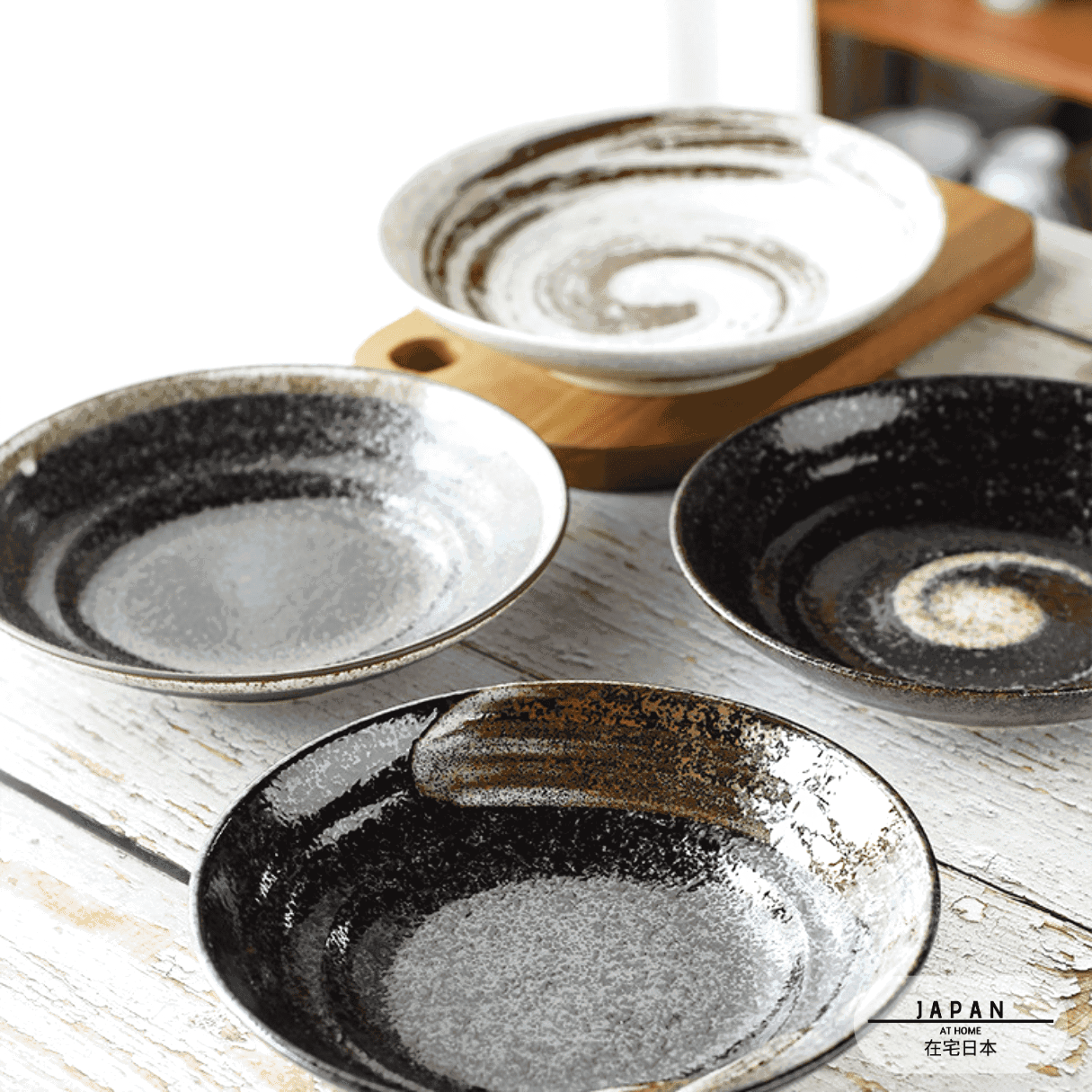 Cinq assiettes creuses Honmono de coloris différents posées sur une table en bois clair