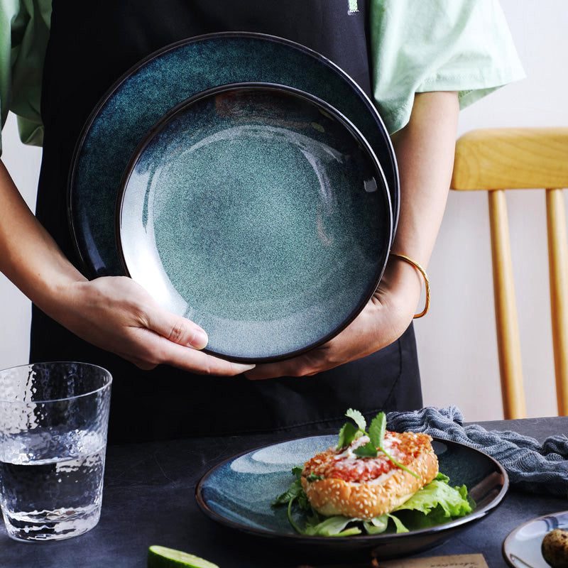 Assiettes bleues en céramique Mihara empilées, tenues en main au-dessus d'une table