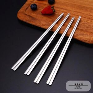 Deux paires de baguettes japonaises en inox sur une planche en bois avec fruits rouges