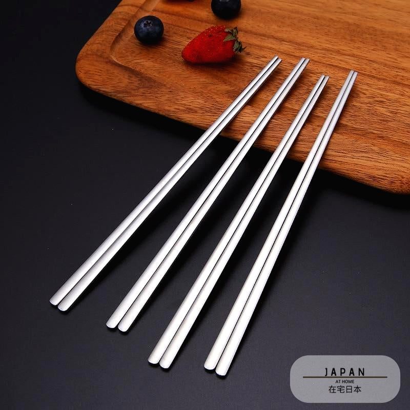 Deux paires de baguettes japonaises en inox sur une planche en bois avec fruits rouges