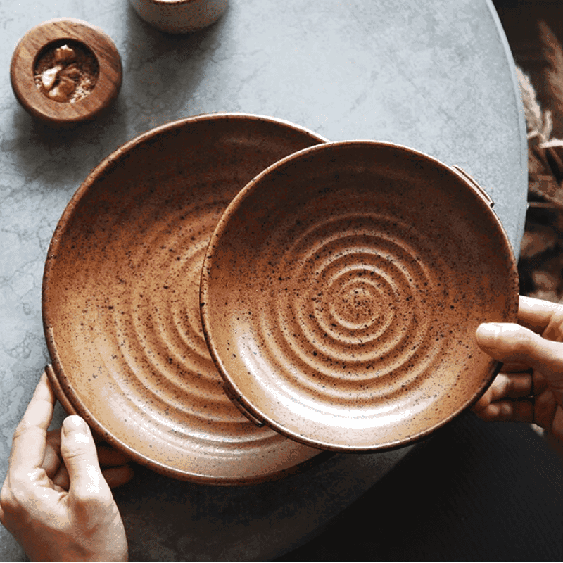 Deux assiettes japonaises Watsuji rouge terre tenues en main au-dessus d'une table