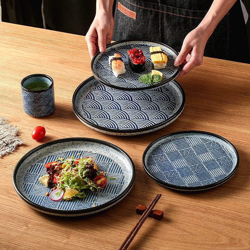 Assiette japonaise Seigaiha garnie de sushis tenue à deux mains au-dessus d'autres assiettes