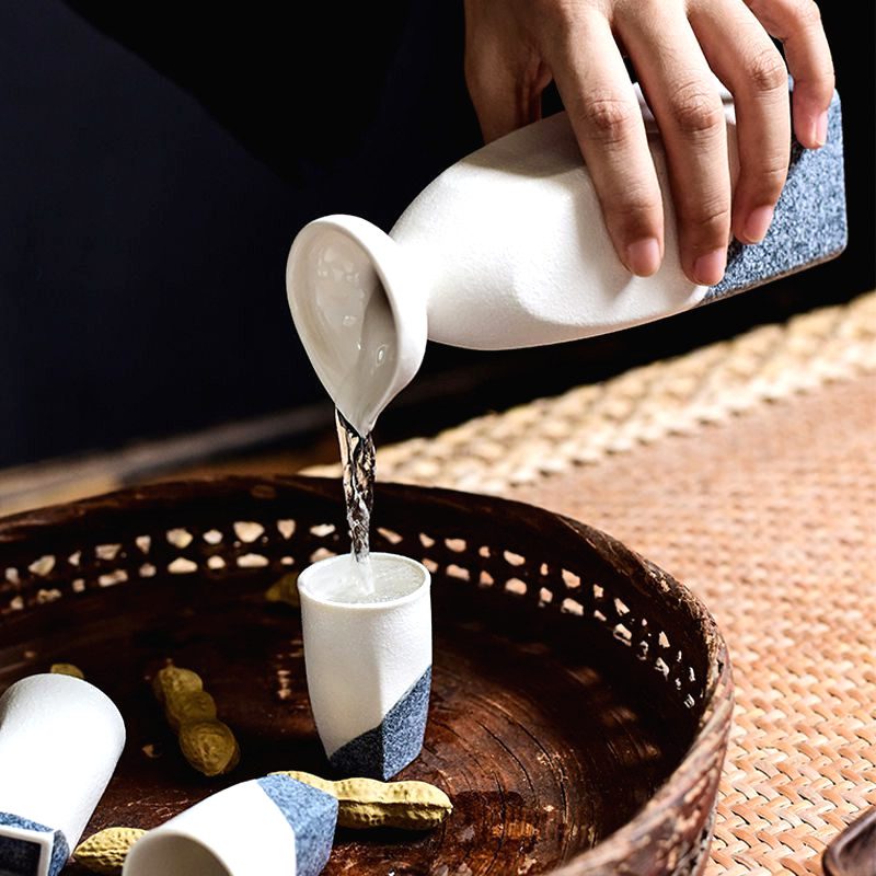 Carafe à saké Iwao versant dans une tasse au-dessus d'un panier