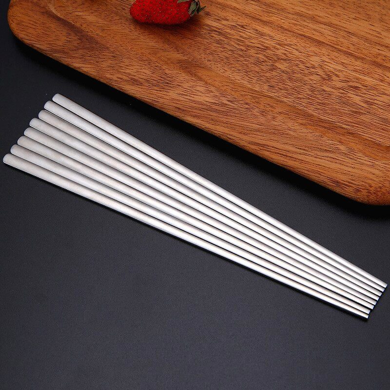 Plusieurs baguettes japonaises en inox alignées sur une planche en bois