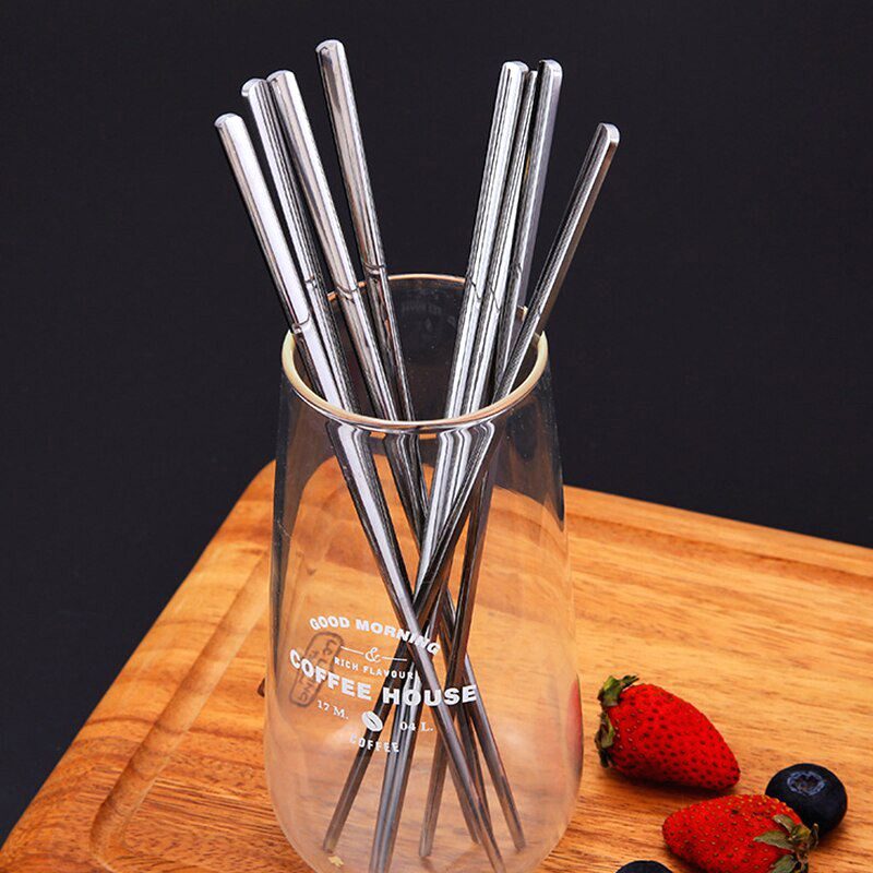 Baguettes japonaises en inox rangées dans un verre sur une planche en bois