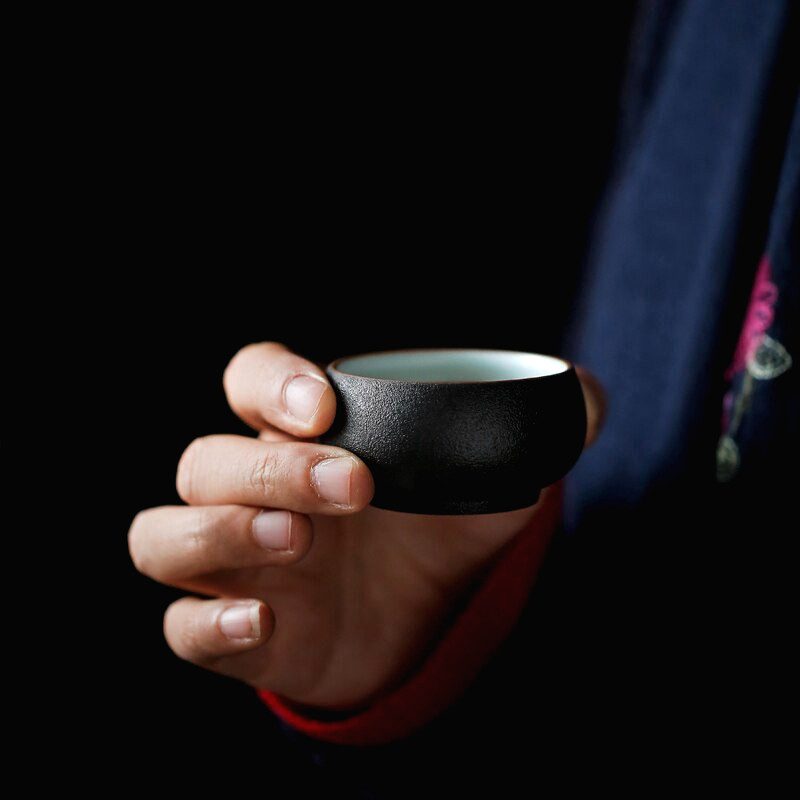 Tasse noire du service à thé Fukui tenue en main