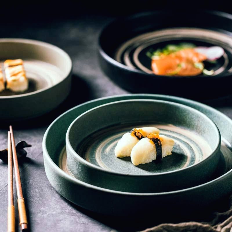 Assiettes japonaises Azami empilées avec sushis et baguettes sur une table sombre