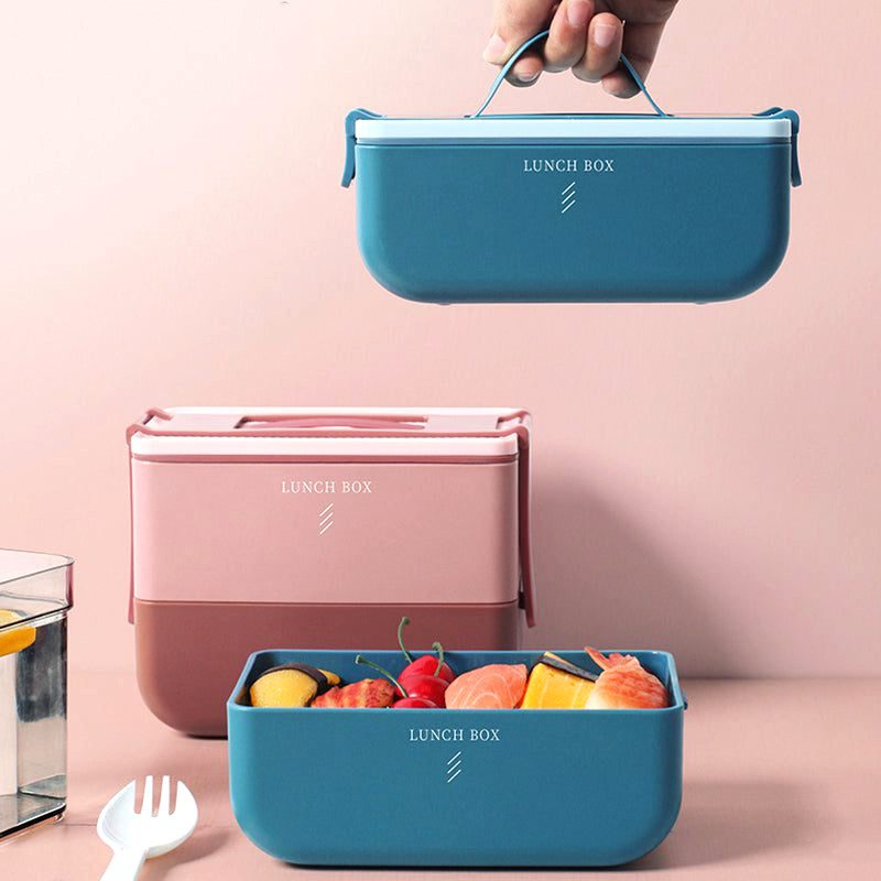 Bento portable bleu tenu par sa poignée au-dessus d'un bento rose garni de fruits