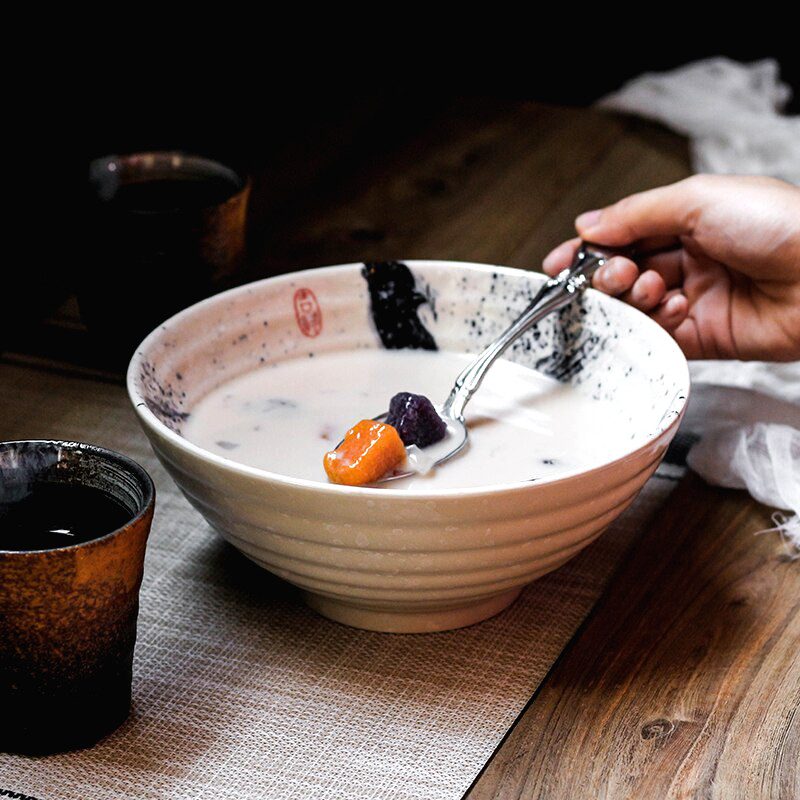 Bol à ramen Tsukuda blanc garni de soupe sur une table en bois, cuillère en main