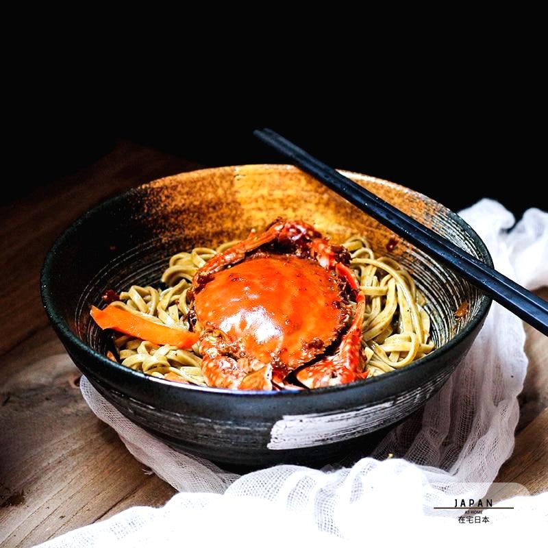 Bol à ramen Tsukuda noir rempli de nouilles et de crabe, baguettes posées
