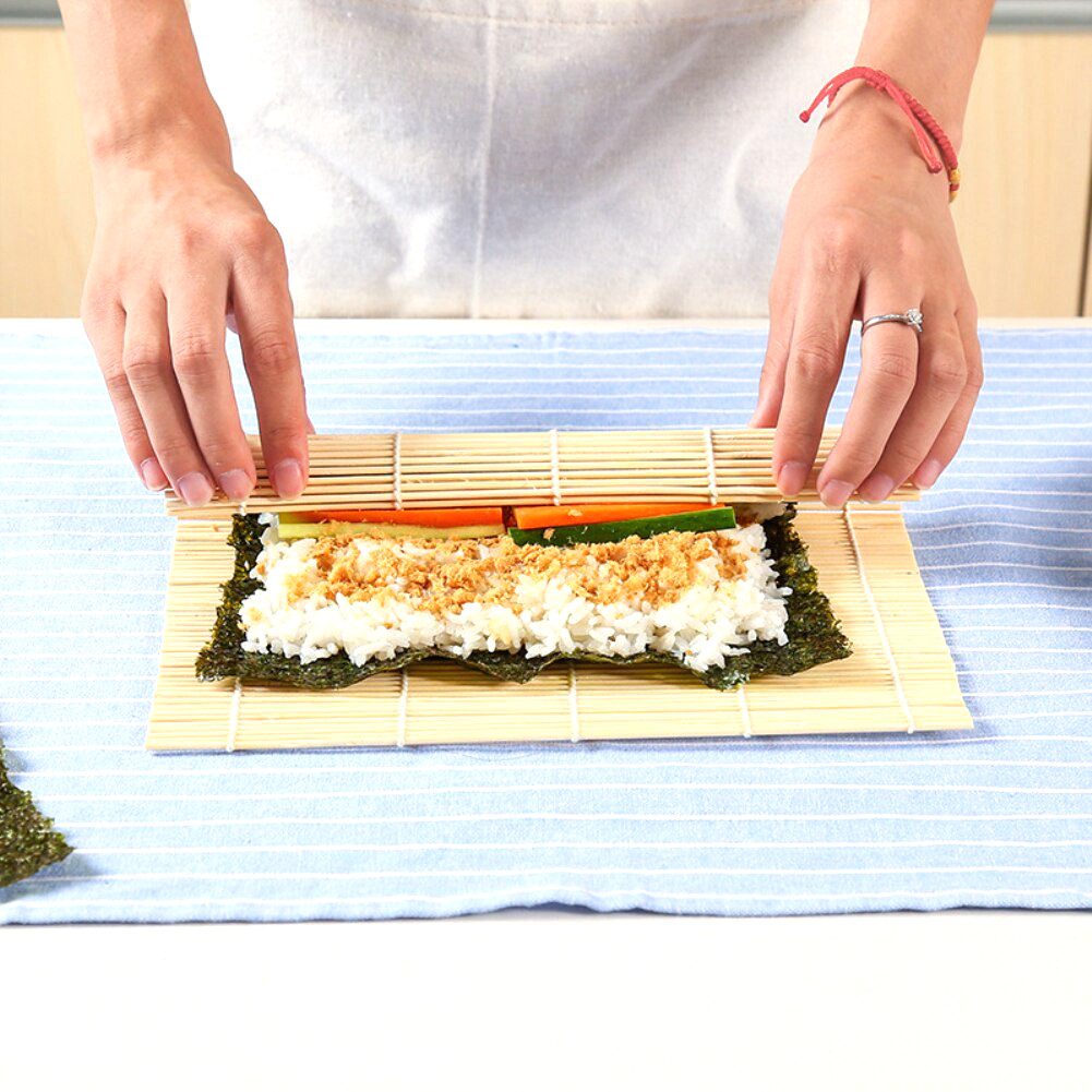 Mains roulant un maki avec la natte à sushi en bambou