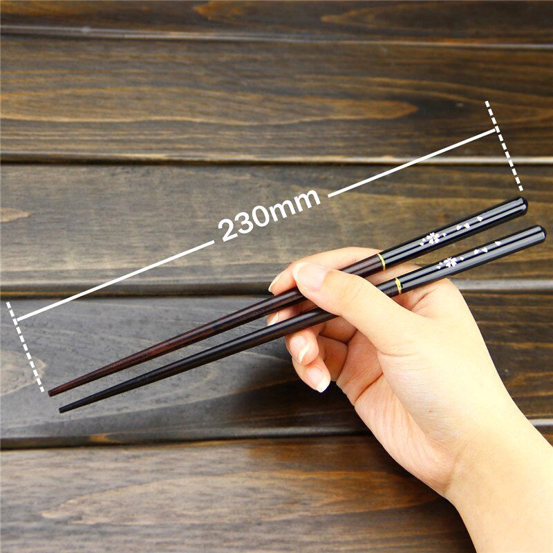 Paire de baguettes en bois laqué tenue en main, avec schéma des dimensions