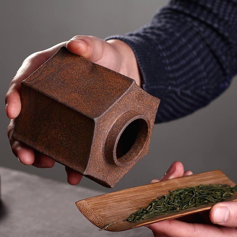 Pot à thé Sunada tenu en main, feuilles de thé versées sur une pelle