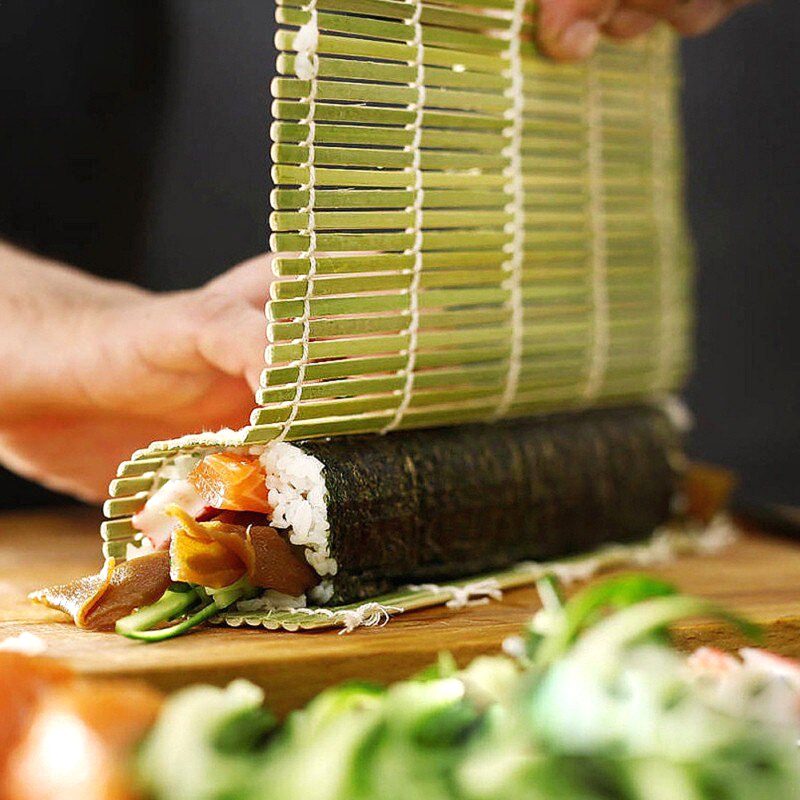 Natte à sushi verte soulevée sur un maki fraîchement roulé