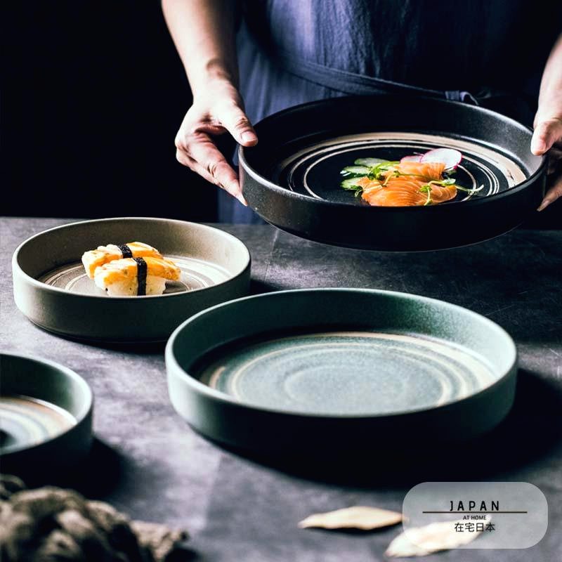 Assiettes japonaises Azami garnies de sushis, l'une tenue à deux mains au-dessus de la table