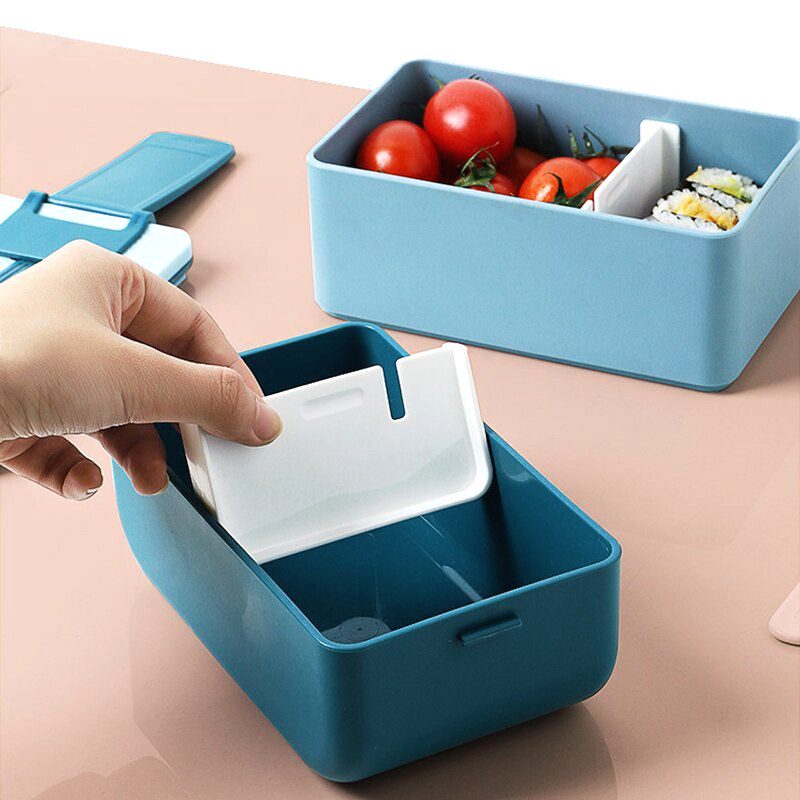 Séparateur amovible glissé dans un bento portable bleu, près d'un autre garni de tomates