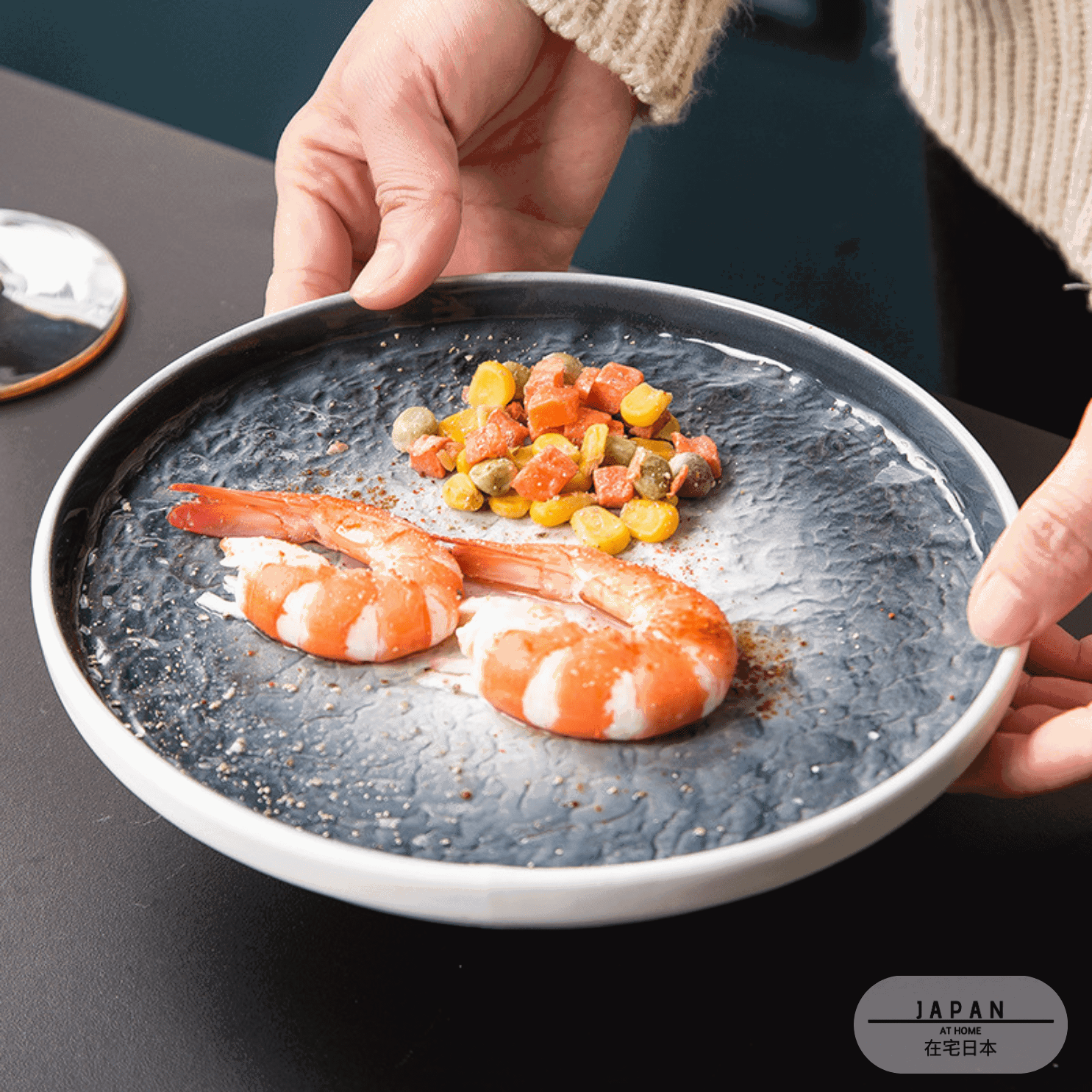 Assiette japonaise Takao bleue garnie de crevettes et dés de légumes, tenue à deux mains