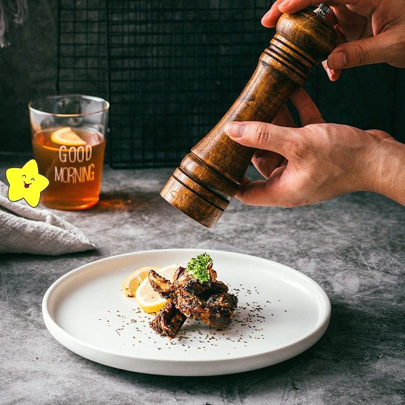 Assiette japonaise Okawa blanche garnie de viande sous un moulin à poivre en bois tenu en main