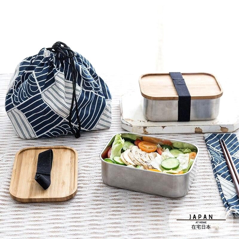 Bento en inox et bambou garni de salade, près d'un sac à motif de vagues