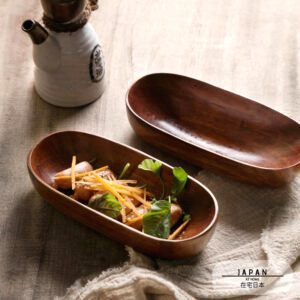 Deux bols canoë en bois d'acacia, l'un garni de légumes, sur un tissu beige