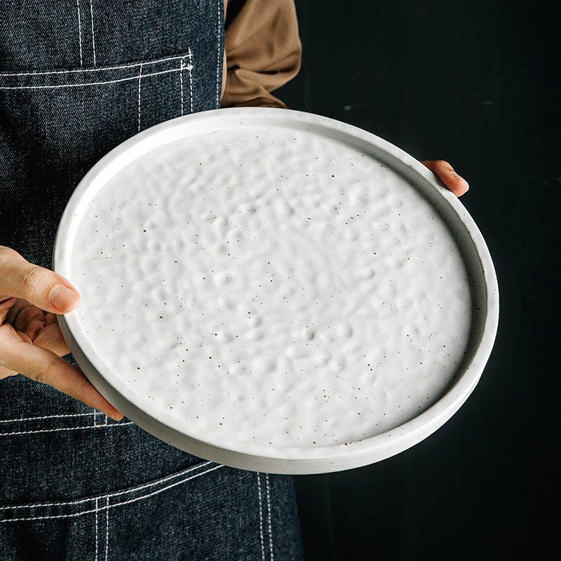 Assiette japonaise Tsuki blanche à relief tenue à deux mains devant un tablier
