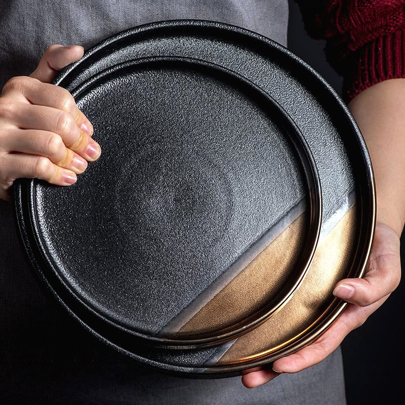 Assiette japonaise Yuna noir et or tenue à deux mains, vue de près