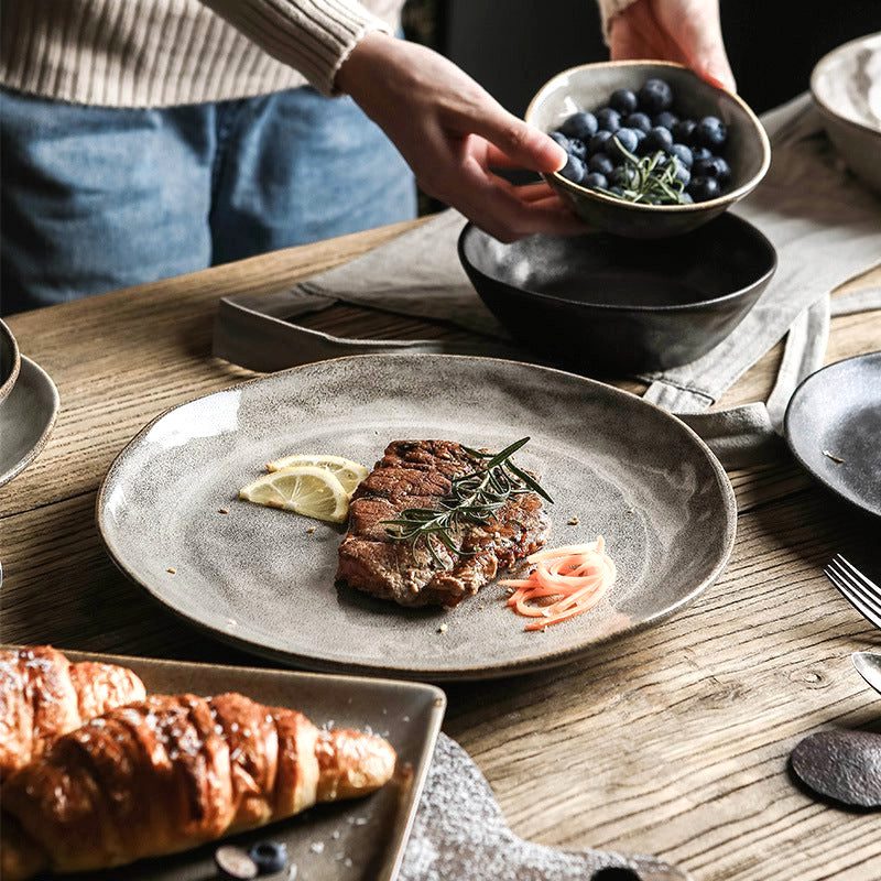 Assiette japonaise Kobo grise garnie de viande et citron, bol de myrtilles tenu en main